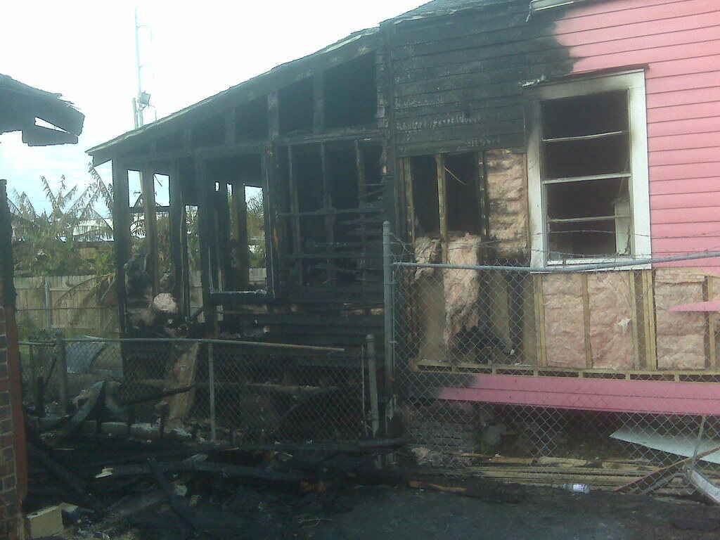 Pink home that has fire damage in the exterior and interior portions of the home. Insulation is exposed and the home is severely damaged
